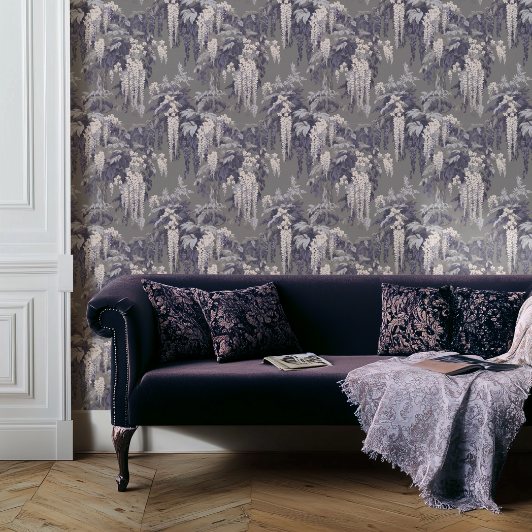 Midnight Wisteria wallpaper in grey and purple with cascading floral pattern styled behind a dark velvet sofa with patterned cushions and a draped throw