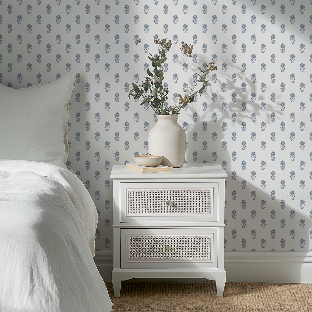 White nightstand with decorative items next to a bed with floral wallpaper.