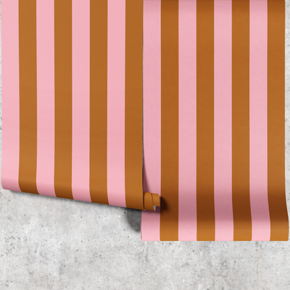 Two panels of pink and gold wide stripe wallpaper hanging against a concrete wall
