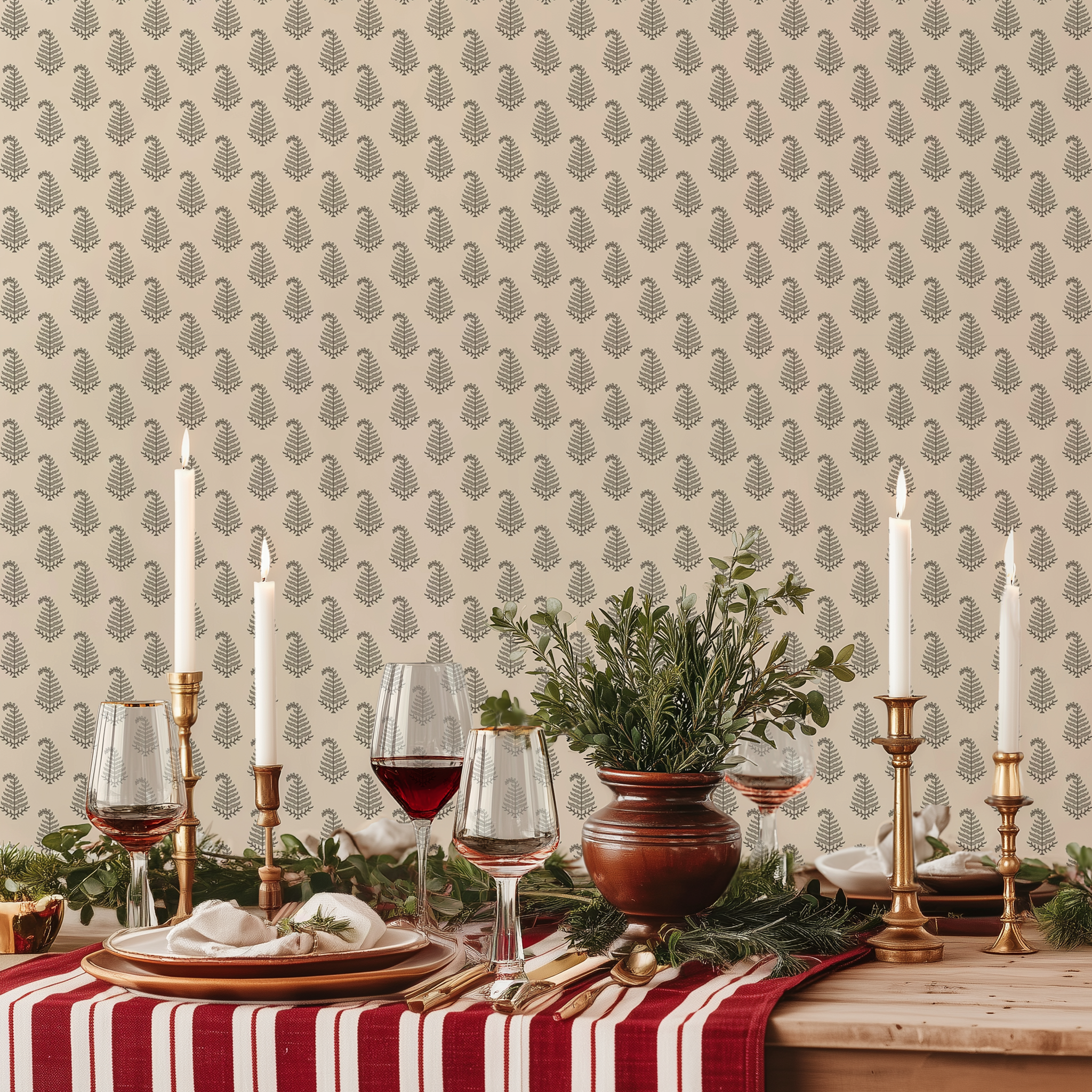 Festive dining table with candles, greenery, and glassware set against a beige wallpaper patterned with small green fern motifs
