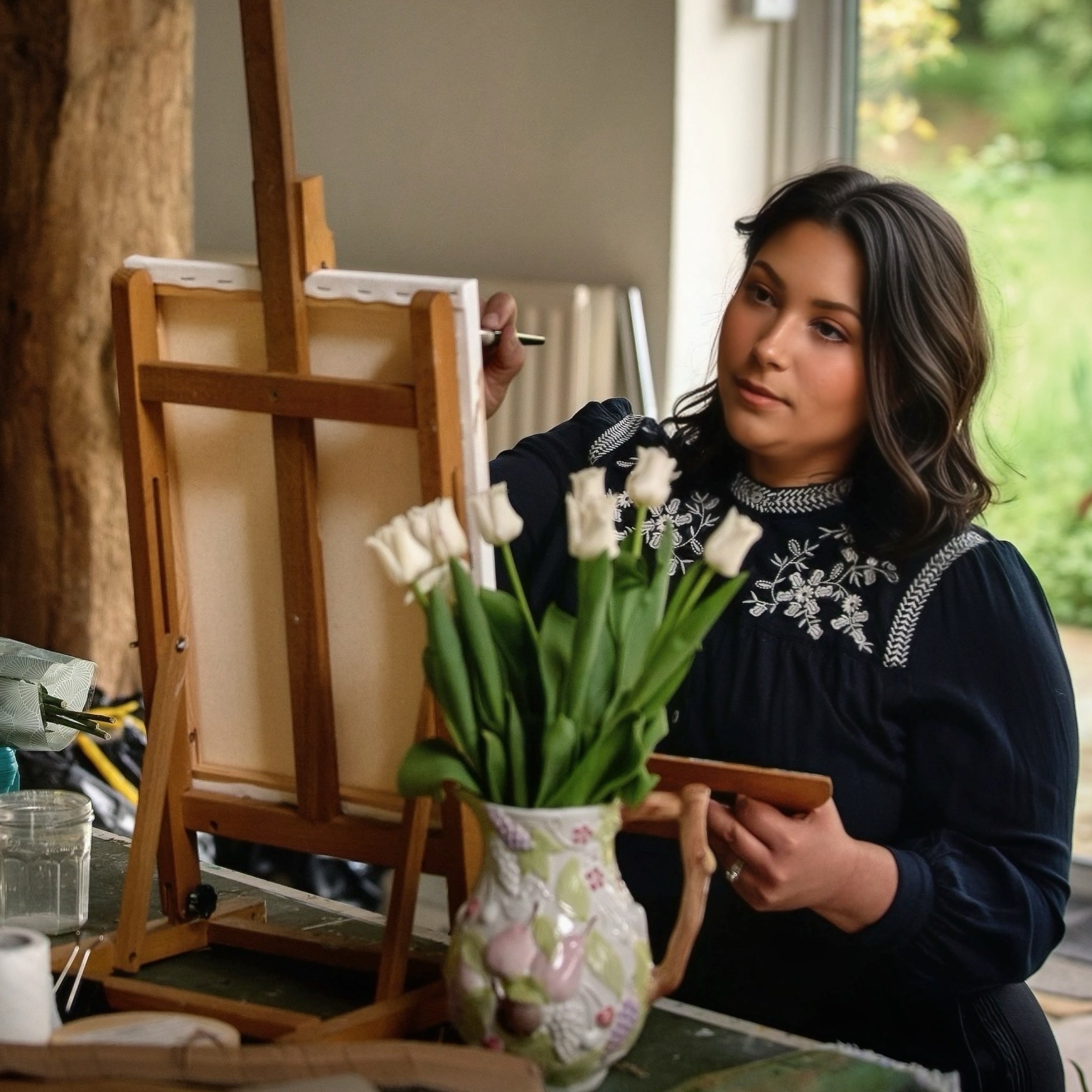 Woman painting a vase of tulips on an easel.