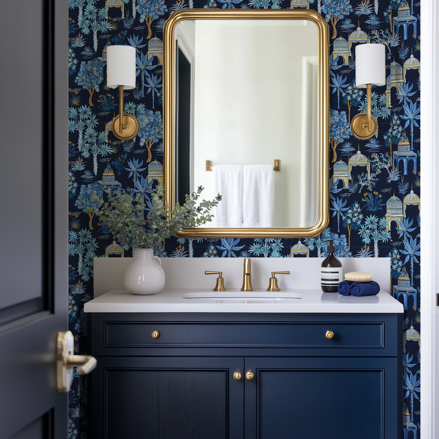 A dark blue vanity in a small powder room, with a gold mirror and dark blue Bali Jungle wallpaper