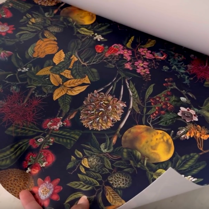 Roll of floral and fruit patterned fabric with a hand holding it open.
