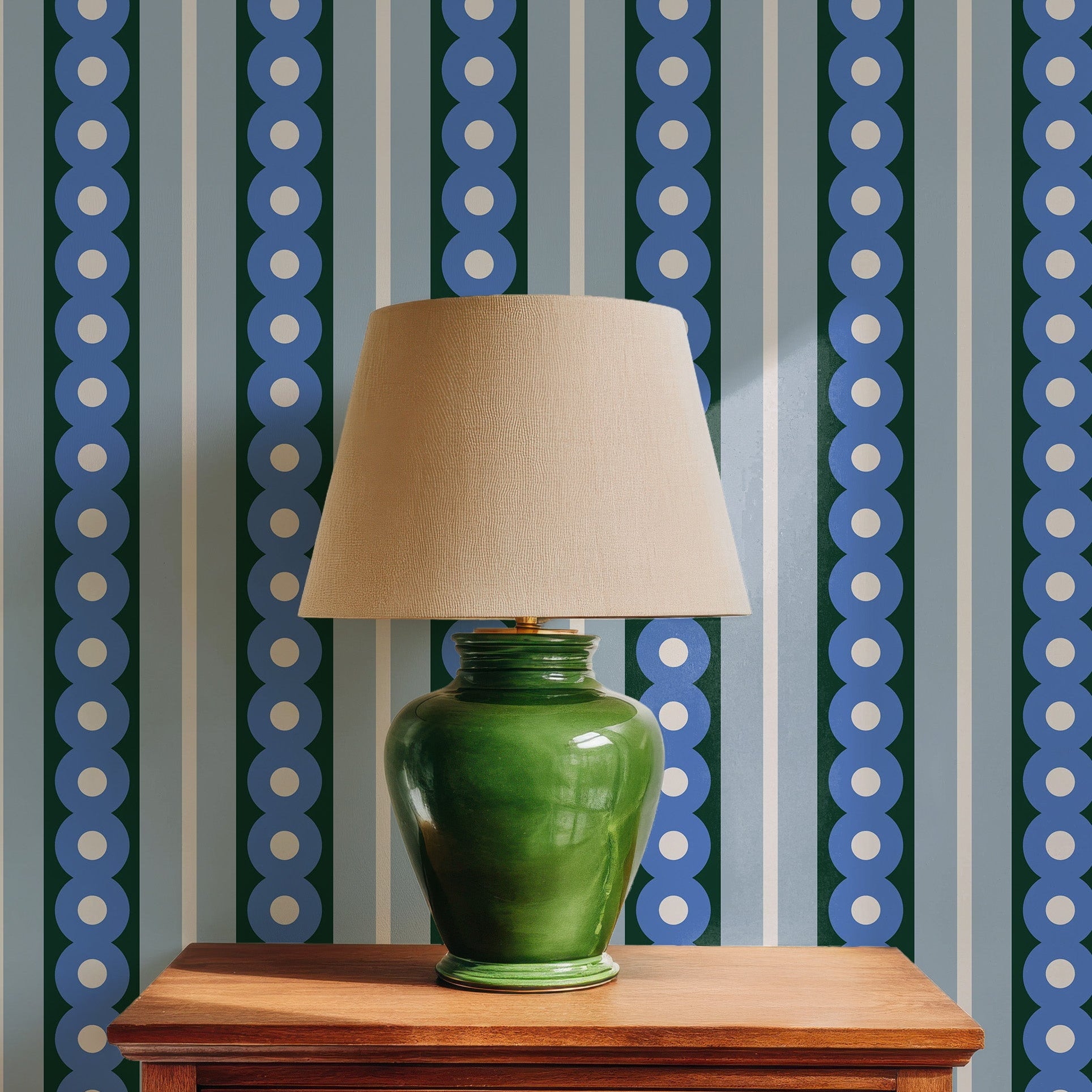 an ambient sunlit image of blue stripes and circles wallpaper behind a wood side table and a green lamp.