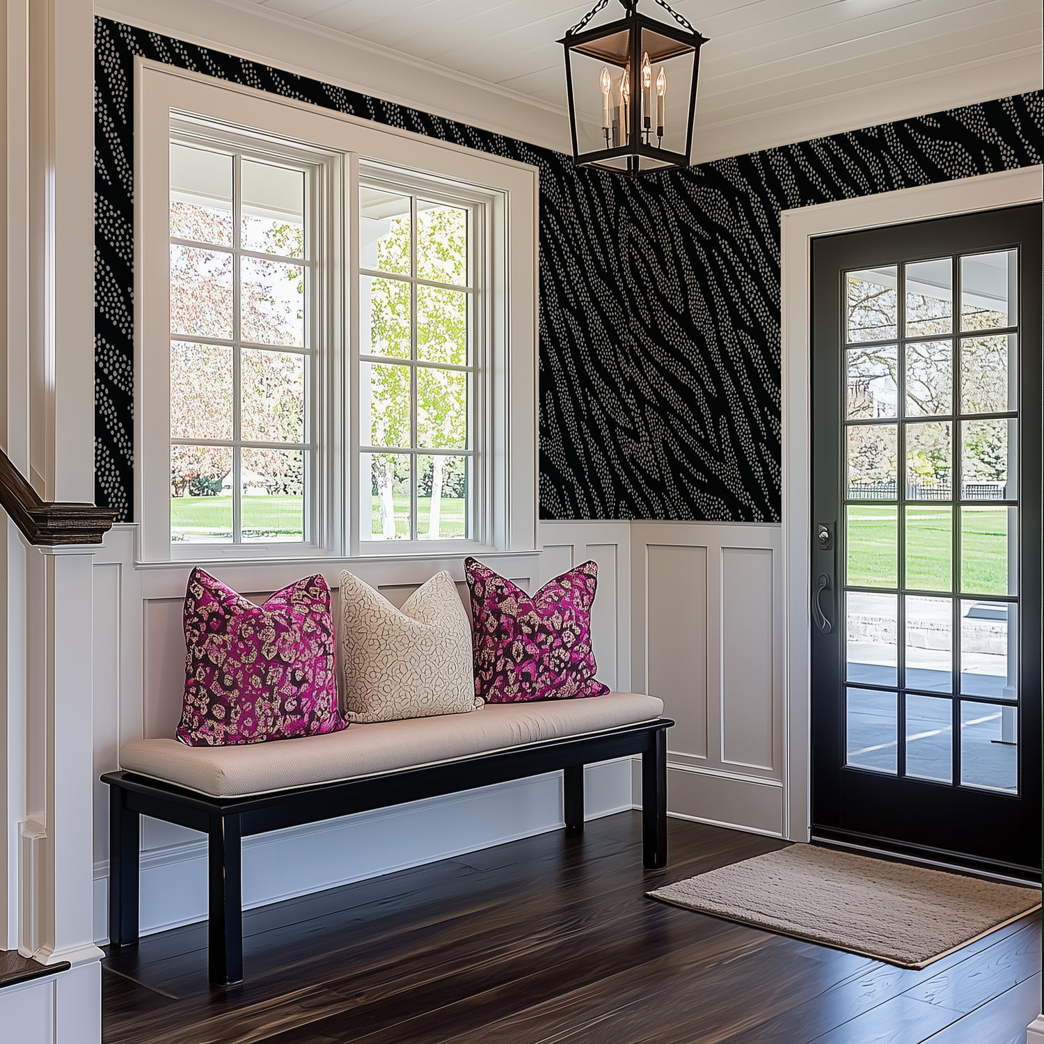 A country entryway with white wainscotting and a modern lack and white dotty animal print wallpaper above it. There is a dark wood bench with cream and pink accent cushions.