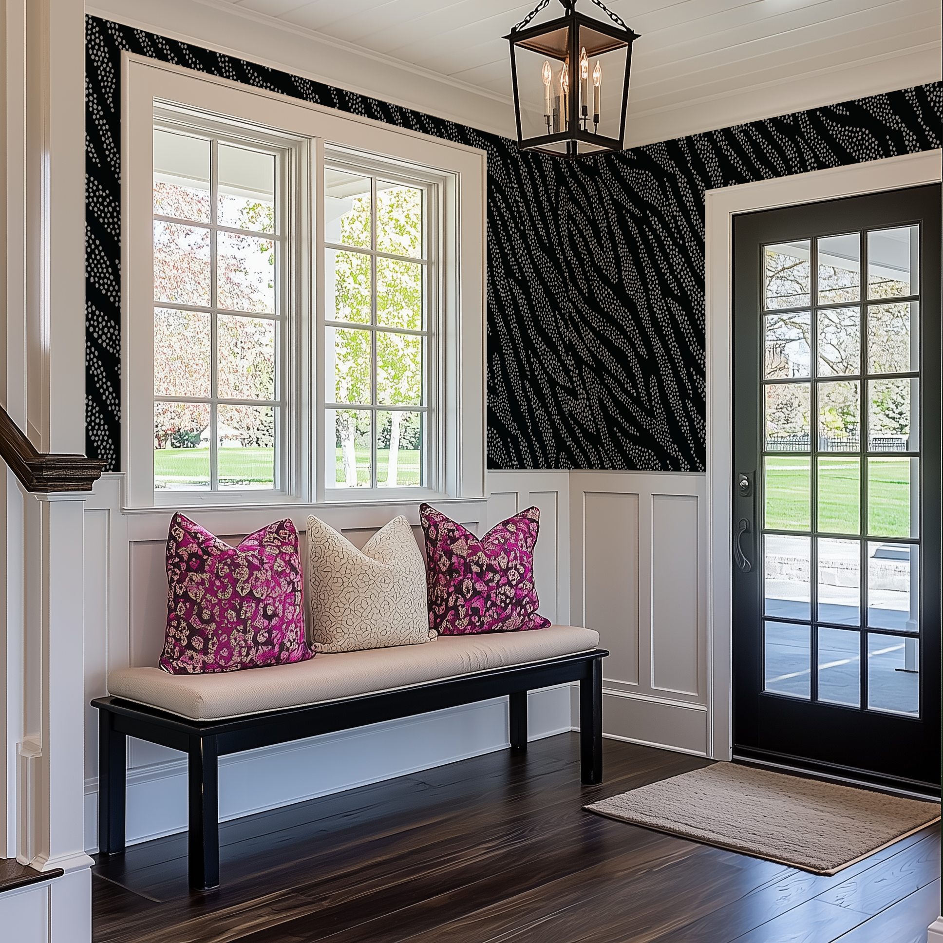 A country entryway with white wainscotting and a modern lack and white dotty animal print wallpaper above it. There is a dark wood bench with cream and pink accent cushions.