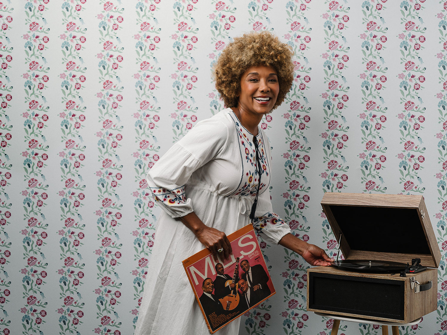 Woman smiling with record player and Gardenia Wallpaper on the wall