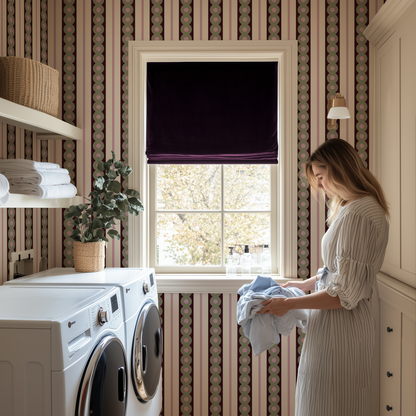 A woman standing in a laundry room that has circles and striped wallpaper and a plum velvet blind at the window