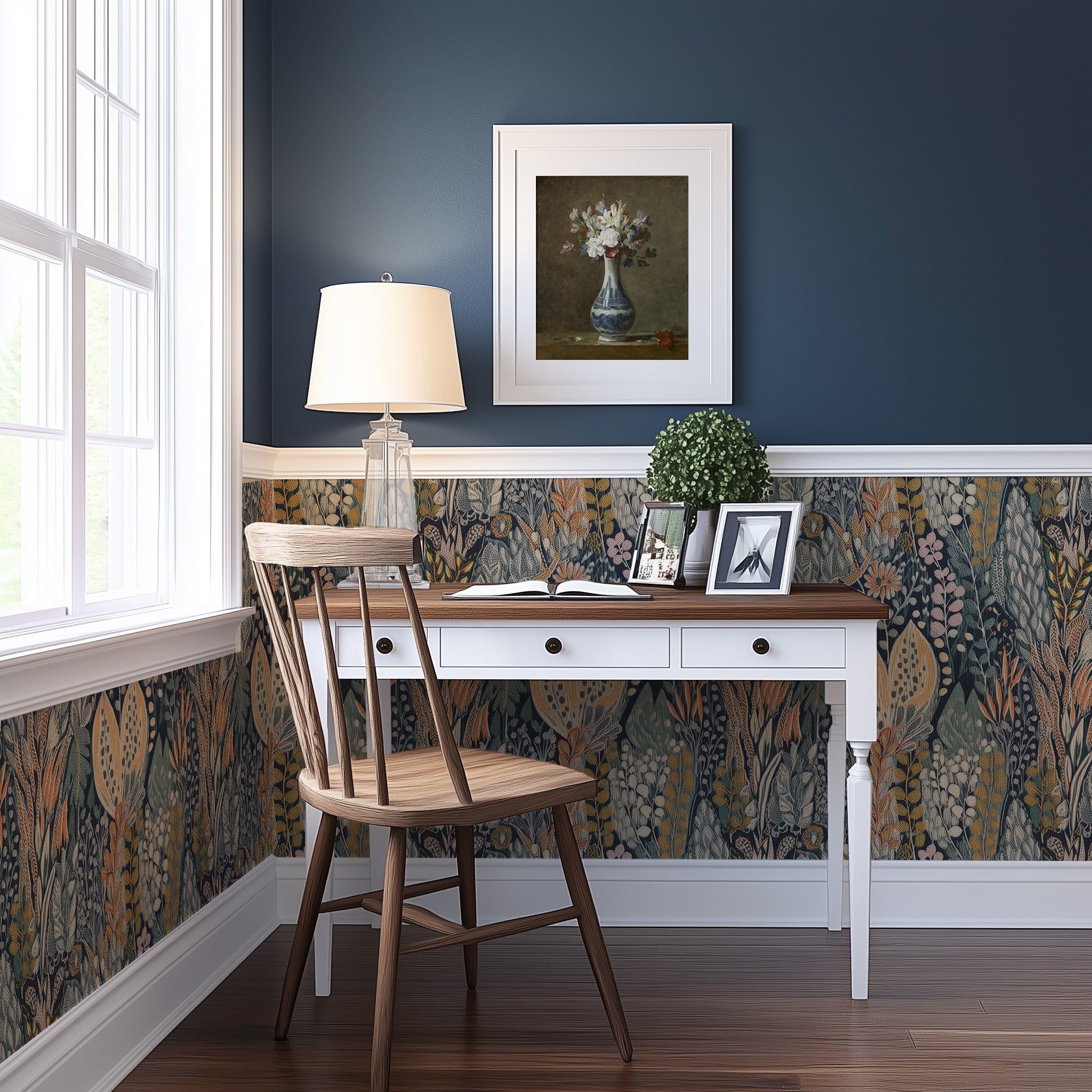 A desk nook in a room with wainscotting where the bottom of the wall is a dark meadow wallpaper an the top of the wall is dark blue