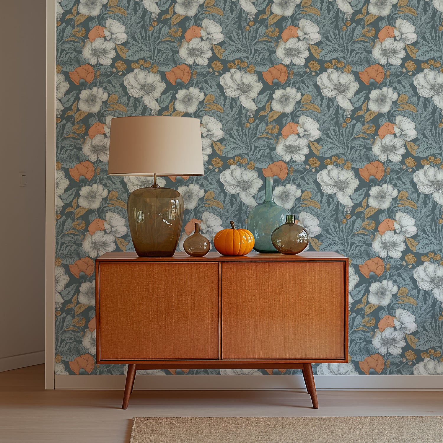 A midcentury dresser with a glass lamp and glass vases in front of a wall with blue poppy wallpaper.