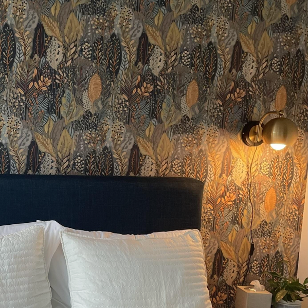 Bedroom with floral wallpaper, white pillows, and a wall sconce.