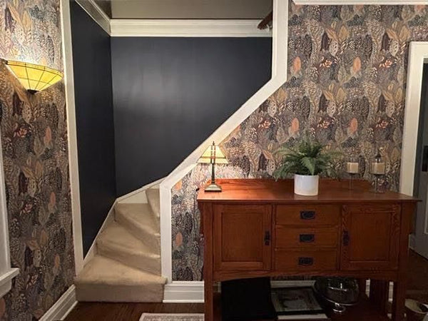 Staircase with patterned wallpaper and wooden sideboard in a room.