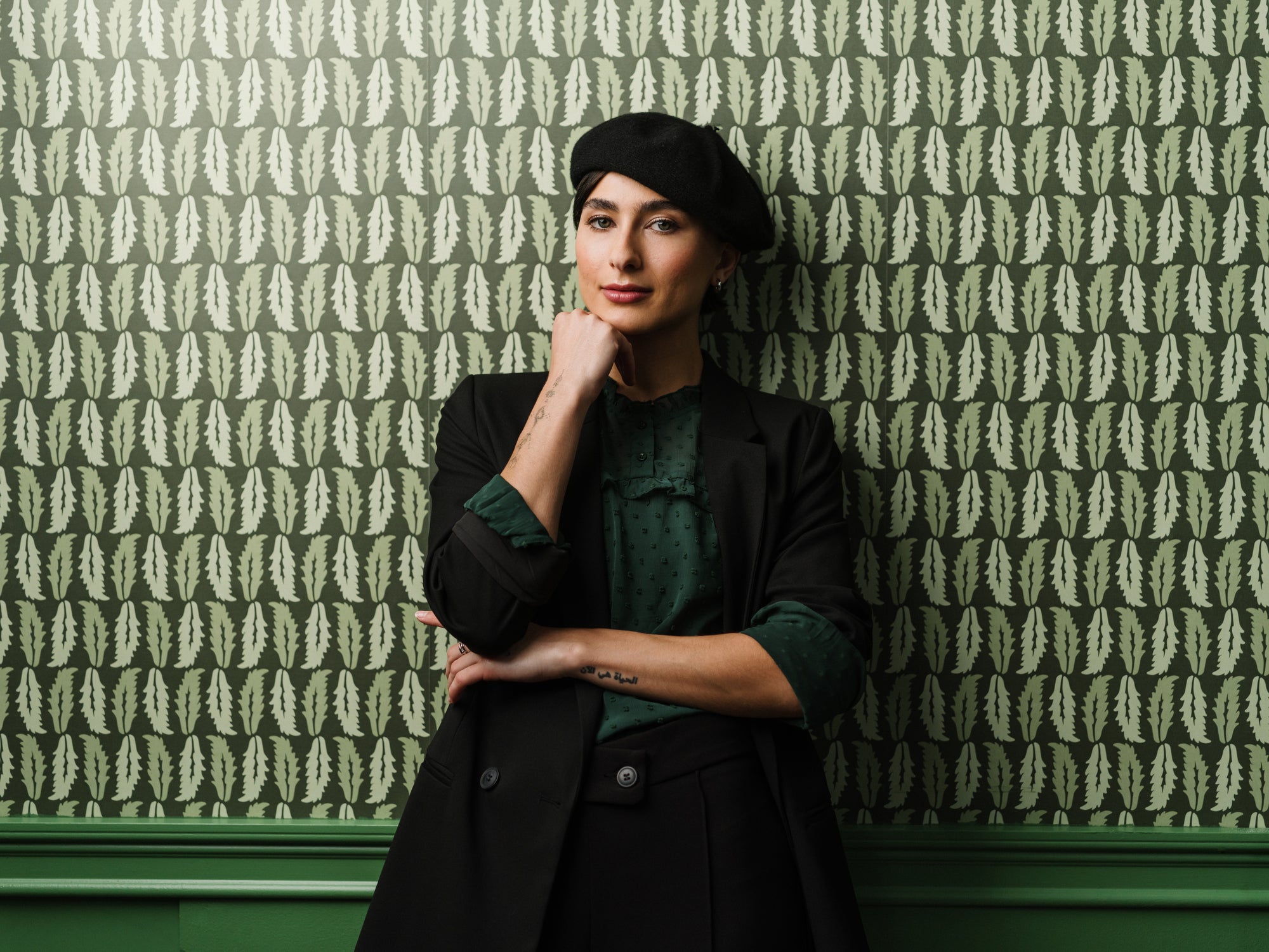 Woman standing against Sweet Chestnut wallpaper in dark green styled in a moody interior